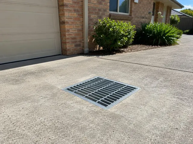 Dry driveway drain grate beside brick house and garage on a paved driveway in Rutherford