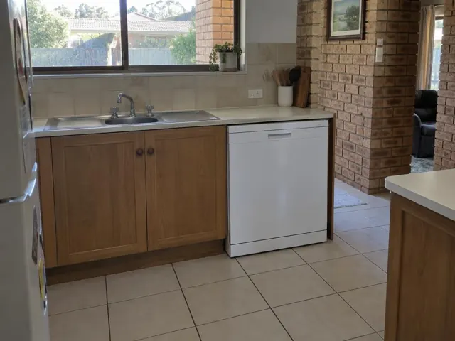 Kitchen with a built-in dishwasher under a laminate benchtop beside a sink and brick wall in Oakhampton Heights