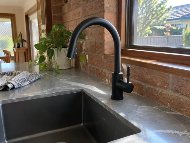 Black kitchen mixer tap beside a stone benchtop and brick splashback, near a window in Rutherford